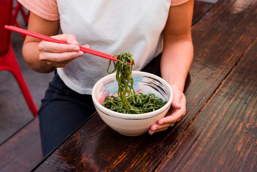close-up-woman-s-hand-eating-green-seaweed-with-red-chopsticks