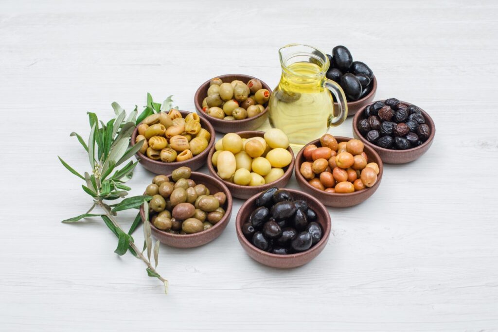 assorted-variety-olives-clay-bowls-with-olive-leaves-jar-olive-oil-high-angle-view-white-wood